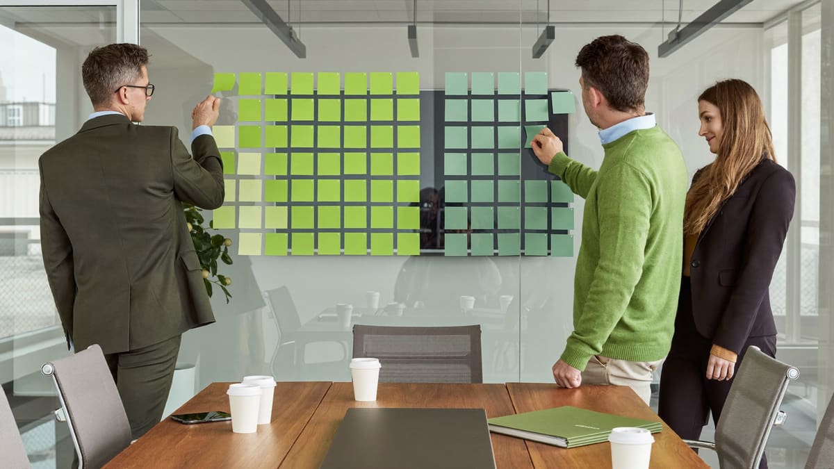 Ein Team sortiert Haftnotizen an einer Wand, um Anforderungen zu vergleichen.